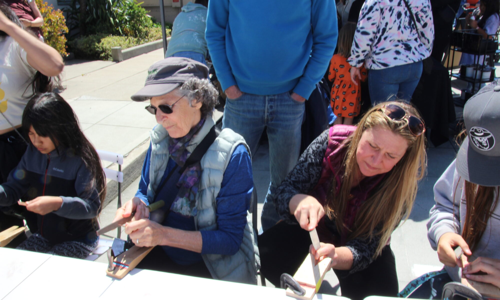 Another view of People of all ages confidently filing the ends of copper pieces to create a bracelet at the Make A Bracelet event as part of the Monterey Museum of Art Block Party 2023