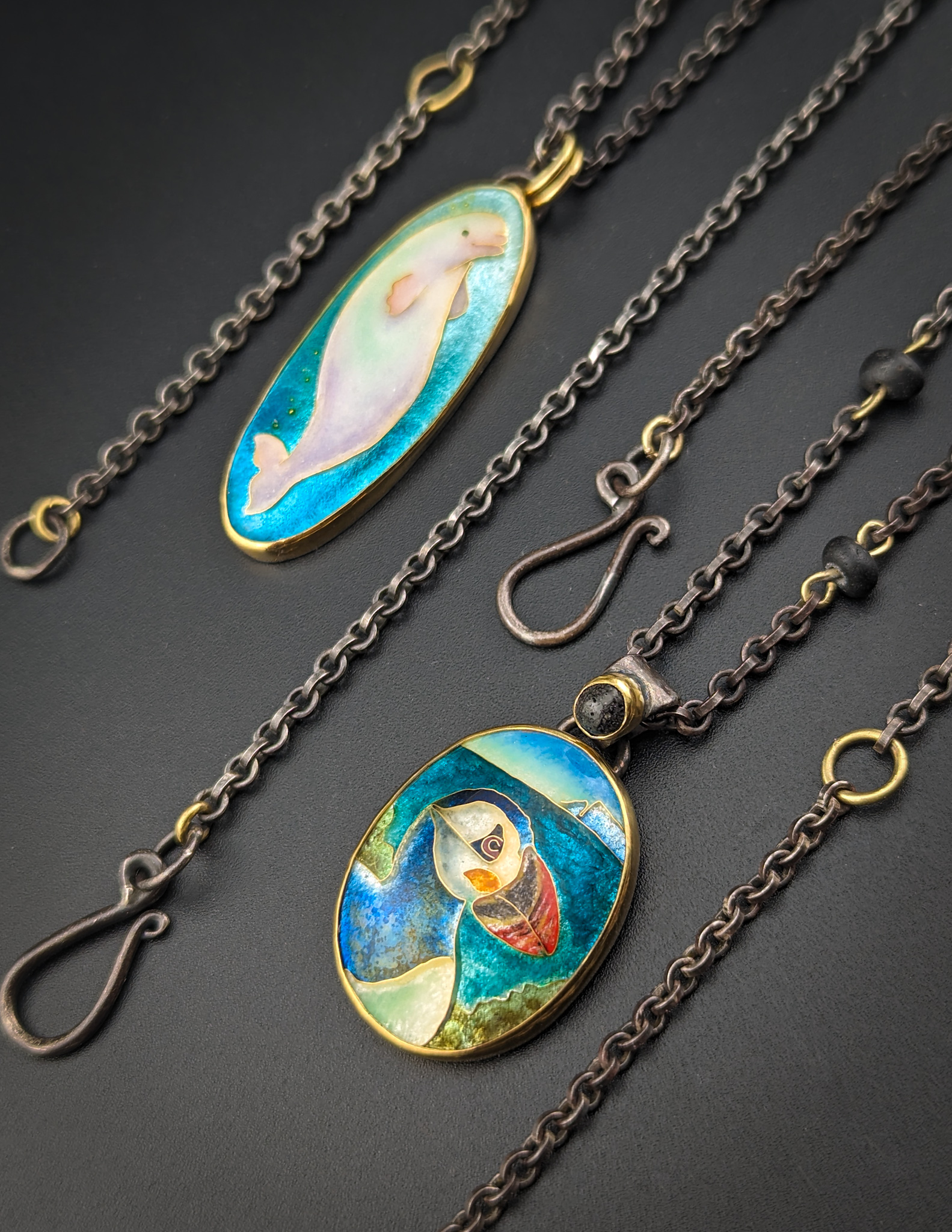 enamel pendants on necklaces by Darci Shea Bogdan. Two oval shapes of marine life in Cloisonne enamel. Displayed on the diagonal.