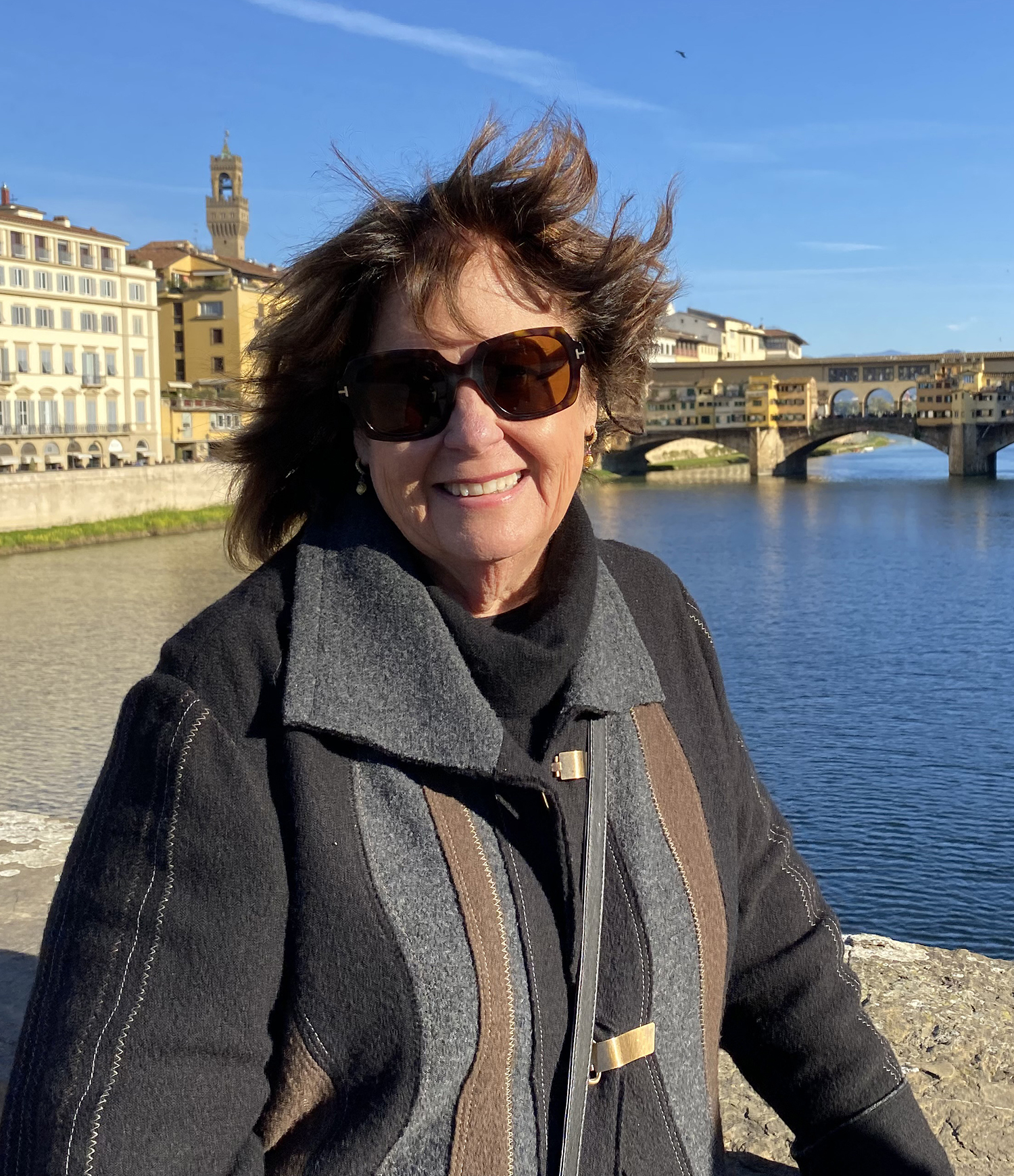 artist and instructor Lynette Cederquist standing on a bridge with a medieval bridge and city buildings behind her